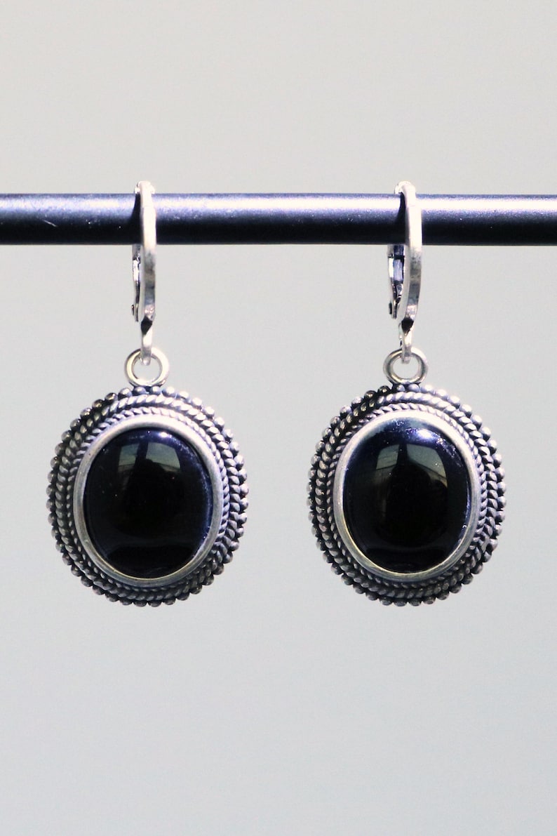 May include: A pair of silver-toned earrings with a black oval stone centre. The earrings have a decorative rope-like border around the stone. The earrings are suspended from a lever back closure.