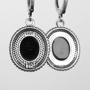 May include: A pair of silver-coloured oval drop earrings. Each earring has a dark oval centre stone, a beaded border, and a decorative outer edge. The earrings are suspended from a simple hoop.