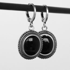 May include: A pair of silver earrings featuring a black, oval gemstone. The earrings have a beaded edge and a lever-back clasp. The jewellery is presented against a plain white backdrop.