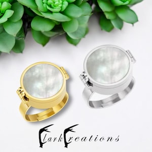 May include: Two round, hinged rings with a white mother-of-pearl inlay. The ring on the left is gold, and the ring on the right is silver. Lark Creations is printed below the rings.
