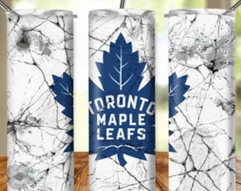 Pode incluir: Um copo de aço inoxidável branco com um design de mármore rachado e um logotipo azul dos Toronto Maple Leafs. O logotipo apresenta uma folha de bordo com o nome da equipe escrito dentro.