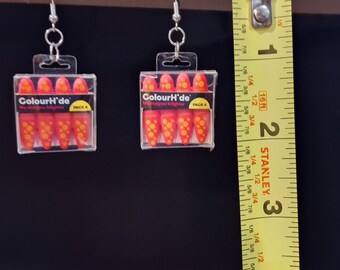 May include: A pair of dangle earrings featuring miniature clear plastic cases containing four orange and yellow highlighter markers labeled ColourH'de. A yellow Stanley measuring tape is positioned next to the earrings, showing a length of 1 inch.