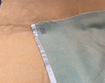 Op de afbeelding: Een gele en groene deken met een witte satijnen rand. De deken heeft een klein label met de tekst "Made in England".
