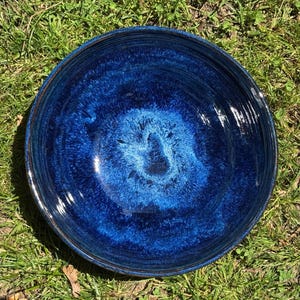 May include: A round ceramic bowl featuring a deep cobalt blue glaze with a lighter, vibrant blue centre. The interior surface displays a mottled, crystalline texture with concentric circular ridges radiating from the base to the wide rim.
