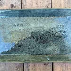 May include: A rectangular ceramic tray with a glossy finish, featuring a mottled color palette of deep forest green, sage, and hints of blue. The surface has a textured, speckled appearance with raised edges and a slightly uneven, organic shape.