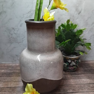 Op de afbeelding: Een witte en bruine keramische vaas met een uitlopende opening. De vaas is gevuld met gele bloemen.