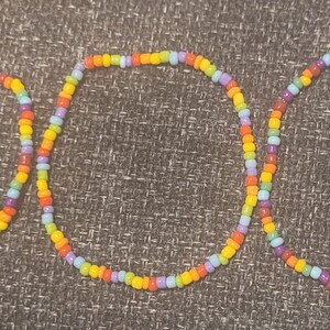 May include: Three colourful beaded bracelets with a rainbow pattern of purple, orange, yellow, and light blue beads.