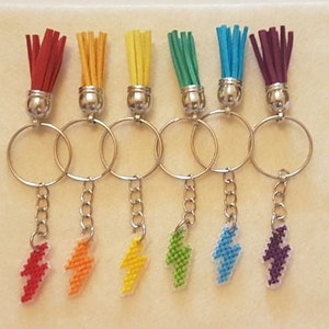 May include: Seven colourful keychains with rainbow tassel charms and silver key rings. Each keychain has a small lightning bolt charm in a matching colour.