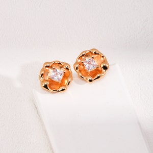 May include: A pair of gold-tone earrings with a square-shaped clear stone set in a textured flower-shaped design.