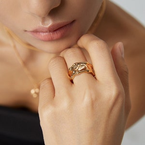 May include: A gold-toned ring with an abstract, organic design. The ring is thick and has a textured surface.