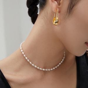 May include: A gold hoop earring with a unique teardrop shape and a delicate pearl necklace.
