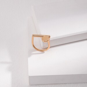 May include: A gold ring with a simple, geometric design. The ring features a thin, horizontal bar and a small, round circle.