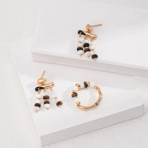 May include: A set of gold earrings with white and brown beads. The earrings are dangling and have a hoop style.