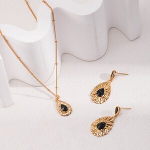 May include: A gold necklace and earrings set with black teardrop-shaped stones surrounded by a delicate, sunburst-like design.