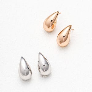 May include: A set of three teardrop-shaped earrings. Two earrings are gold and one earring is silver.