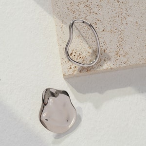 May include: A pair of silver abstract earrings. One earring is a smooth, rounded shape, while the other is a thin, open circle.