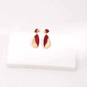 May include: A pair of gold earrings with a red and gold teardrop design.