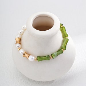 May include: A bracelet made of white pearls, green and white bamboo-shaped beads, and gold accents.