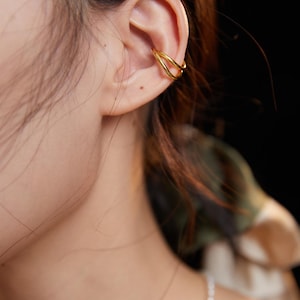 May include: A gold ear cuff with a double-loop design. The cuff is worn on the upper part of the ear.