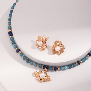 May include: A gold necklace with a blue and dark blue beaded chain and a gold pendant with a pearl. Matching gold earrings with pearls.
