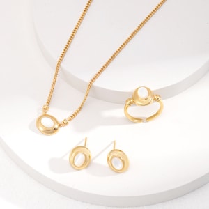 May include: A gold necklace, ring, and earrings set with oval-shaped white stones. The jewelry features a delicate gold chain and a simple design.
