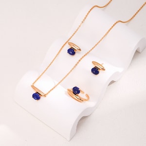 May include: A gold necklace, ring, and earrings set with blue oval-shaped stones. The jewelry is displayed on a white surface.