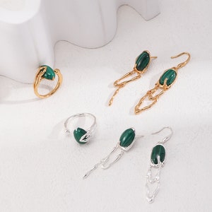 May include: A set of four jewelry pieces featuring green malachite stones. Two pairs of earrings with dangling chains and two rings with a leaf design.