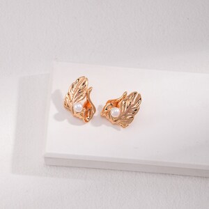 May include: A pair of gold-tone earrings with a leaf design and a small pearl accent.