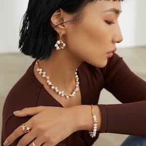May include: A set of gold-toned jewelry featuring a pearl necklace, bracelet, and earrings. The necklace and bracelet are made of small, irregular pearls and gold beads. The earrings are circular and feature a cluster of pearls.
