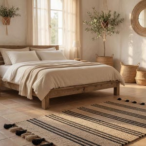 Peut inclure: Une chambre à coucher avec un lit en bois, une literie de couleur neutre et un tapis rayé à pompons. La pièce a une palette de couleurs neutres, avec la lumière naturelle traversant une grande fenêtre. Des plantes décoratives et un miroir complètent l'ambiance.
