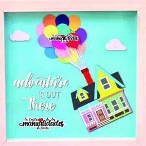 May include: A framed picture with a light blue background featuring a house with balloons. The house is yellow and pink with white trim. The balloons are multi-coloured and have a string attached to them. The text "adventure is out there" is written in white on a black background. The text "La Casita de las Manualidades de Carla" is written in white on a red background.