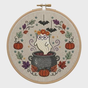 Peut inclure: Un tambour à broder circulaire contenant un tissu en lin avec un motif brodé d'un fantôme blanc portant une couronne de fleurs et des lunettes violettes, sortant d'un chaudron gris foncé, entouré de citrouilles orange, de feuilles d'automne et de chauves-souris.