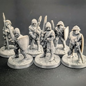 Puede incluir: Un conjunto de siete figuras en miniatura de plástico gris de soldados medievales, cada uno con un arma y un escudo, de pie sobre bases redondas.