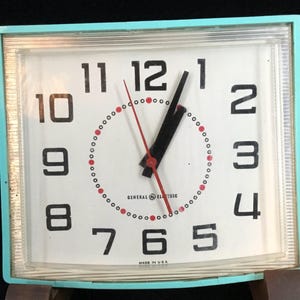 May include: Vintage General Electric clock with a rectangular turquoise frame. The white face features black numerals, a red second hand, and black hour and minute hands. The clock reads "Made in USA".