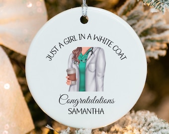 Könnte beinhalten: Weißer Keramik-Anhänger mit einer grün-weißen Illustration einer Person in einem weißen Kittel, die eine Tasse Kaffee hält. Der Text lautet "Just a girl in a white coat. Congratulations Samantha."