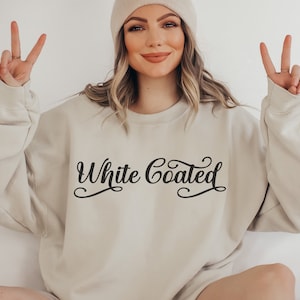 May include: A beige sweatshirt with the text "White Coated" in black cursive lettering.