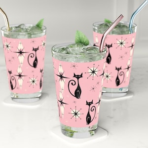 Pode incluir: Três copos cor-de-rosa com gatos pretos e estrelas brancas. Os copos estão cheios de um líquido transparente e têm palhinhas. O texto "ORIGINAL DESIGN" está na parte inferior da imagem.