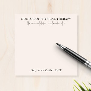 May include: A white notepad with the text "DOCTOR OF PHYSICAL THERAPY Like a normal doctor except much cooler" and "Dr. Jessica Zeitler, DPT" printed on it. The notepad is on a light wood surface with a pen and a potted plant.