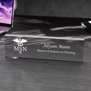 May include: A clear glass desk nameplate with a white caduceus symbol and the text "MSN" above the name "Allyson Mann" and the text "Master of Science in Nursing".