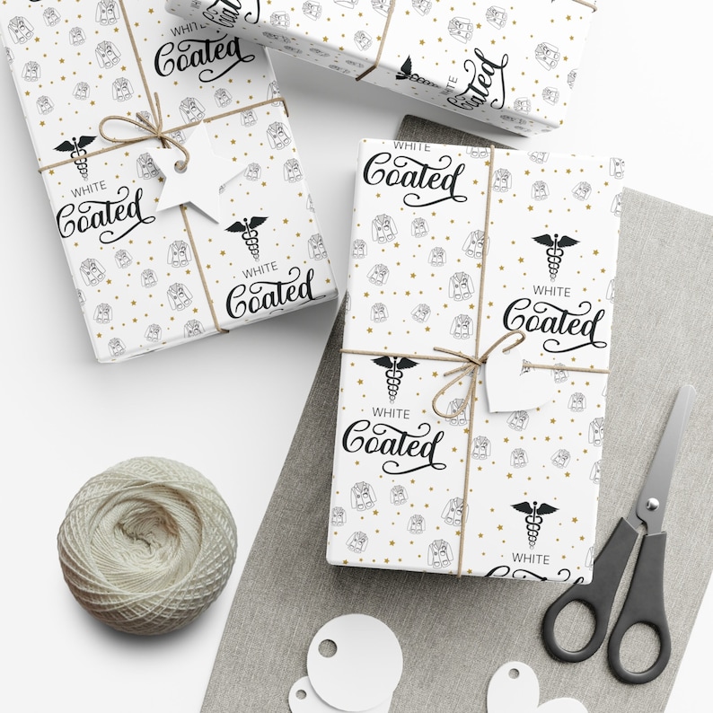 K&ouml;nnte beinhalten: Wei&szlig;es Geschenkpapier mit einem sich wiederholenden Muster aus goldenen Sternen und einer Schwarzwei&szlig;illustration eines Arztkittels und eines Caduceus. Der Text "WHITE Coated" wird auf dem Papier wiederholt.