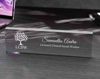 May include: A clear acrylic desk nameplate with a white tree design and the text "Samantha Andra, Licensed Clinical Social Worker, LCSW".