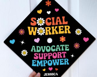 May include: Black graduation cap with colorful text: "SOCIAL WORKER ADVOCATE SUPPORT EMPOWER" and the name "JESSICA 2026". The design includes flowers, hearts, and stars. A graduation cap for a social worker.