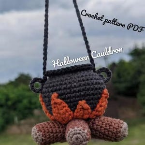 May include: A crocheted dark gray cauldron with orange flames and brown logs at the base, suspended by a black yarn strap. The text Crochet pattern PDF, Halloween Cauldron, and Yarnproductsua are visible on the image.
