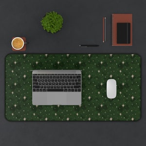 May include: A green desk mat with a white star pattern. A laptop computer, a white mouse, and a cup of coffee are on the mat.