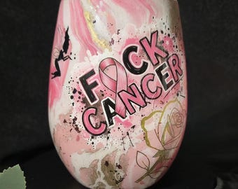Op de afbeelding: Een steelvrije beker met een roze, witte en gouden marmerafwerking. Het ontwerp bevat de zwarte tekst FOCK CANCER met een roze lint dat de letter O vervangt, een zwart silhouet van een fee en een illustratie van een roze roos met gouden rand.