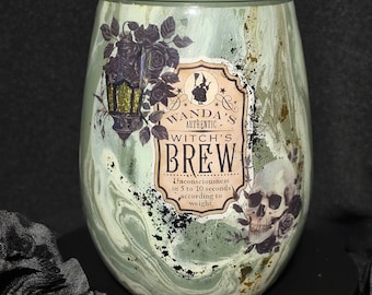 Op de afbeelding: Een glas zonder steel met een gemarmerde afwerking in saliegroen en wit. De voorzijde heeft een etiket met de tekst Wanda's Authentic Witch's Brew, Unconsciousness in 5 to 10 seconds according to weight, naast illustraties van een schedel, rozen en een lantaarn.