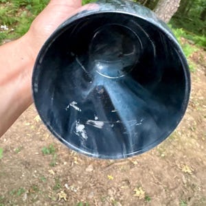 May include: A cylindrical cup with a deep black base color featuring swirling white marble-like patterns throughout the interior and exterior walls. The vessel has a wide circular opening and a smooth, polished finish on the surface.