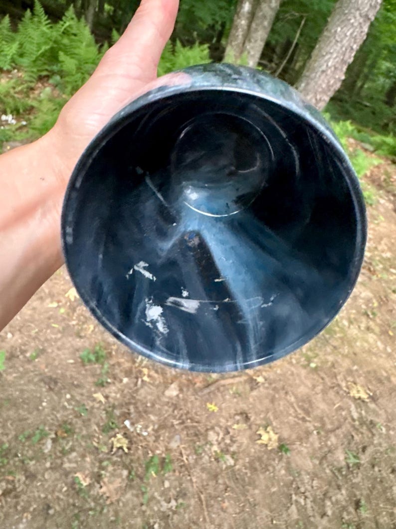 May include: A cylindrical cup with a deep black base color featuring swirling white marble-like patterns throughout the interior and exterior walls. The vessel has a wide circular opening and a smooth, polished finish on the surface.