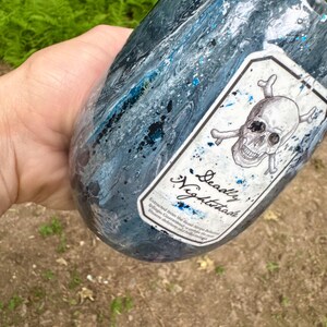 May include: A dark blue and black marbled tumbler featuring a white rectangular label with a skull and crossbones illustration. The label includes the text Deadly Nightshade and smaller printed text below. The surface has a glossy finish.