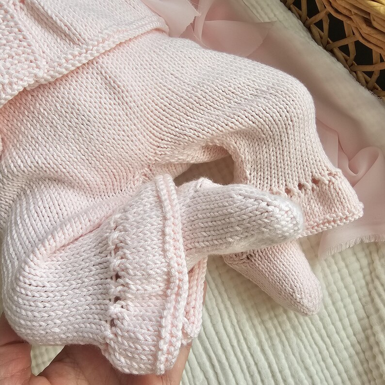 May include: A pink knitted baby outfit with a long-sleeved top and pants. The outfit has a delicate knit pattern and is perfect for a newborn.